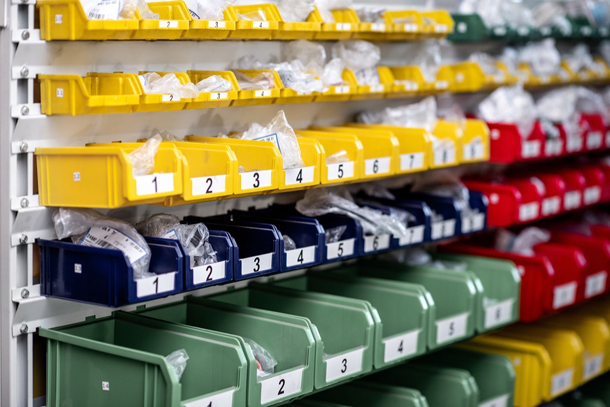 Rows of numbered yellow, blue, red and green parts bins holding bagged components on a stores rack