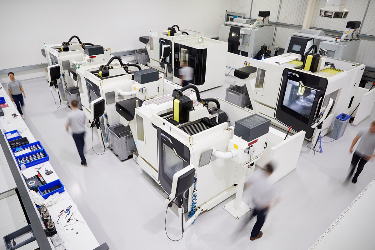 Overhead view of a bright CNC machining workshop with rows of white machining centres and staff walking between them