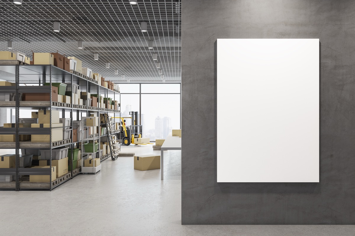 Modern warehouse interior with steel racking, a forklift and a blank white notice board mounted on a concrete wall, with no people in view
